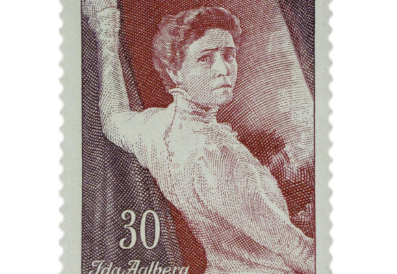 Pystymallinen punamusta postimerkki, jossa nainen on kiinni verhossa, eteenpäin menossa, mutta katsoo taakseen. Ylhäällä tekstinä Suomi Finland. Alhaalla vasemmalla kolmekymmentä numeroin sekä Ida Aalberg 1857-1957.