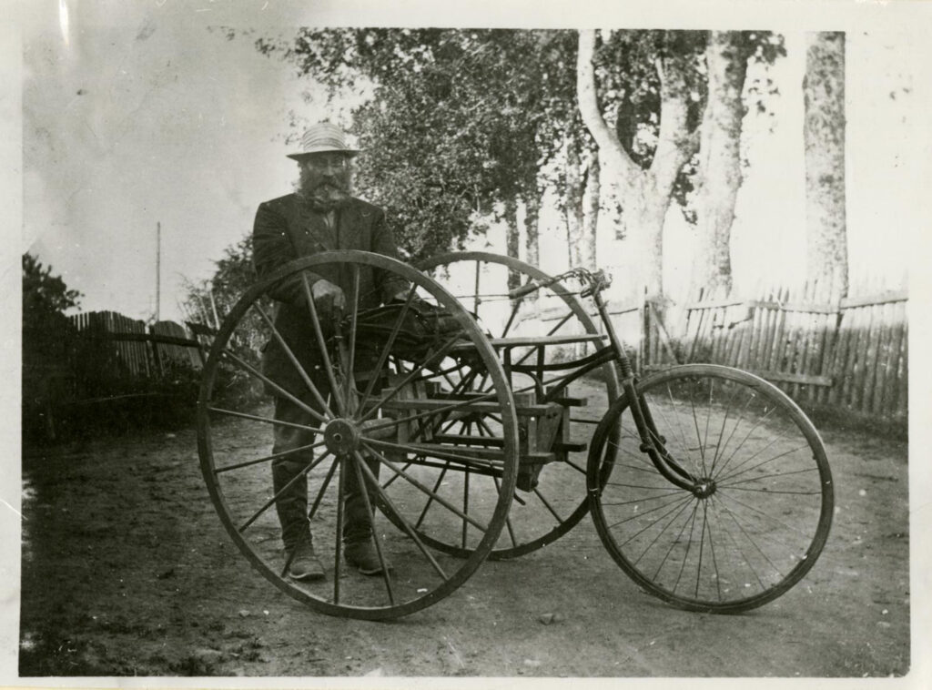 Kolmirenkainen pyörä ja postinkantaja mustavalkokuvassa.